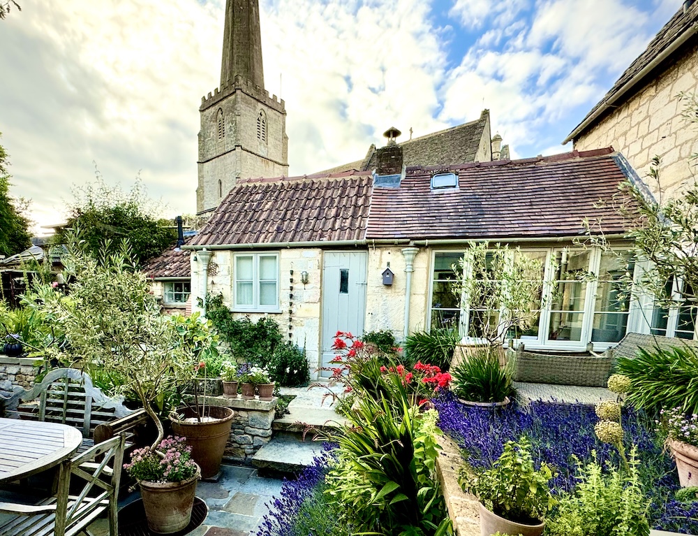 A pretty cottage garden in Painswick with the steeple of St Mary's in the background, Gloucestershire, the Cotswolds